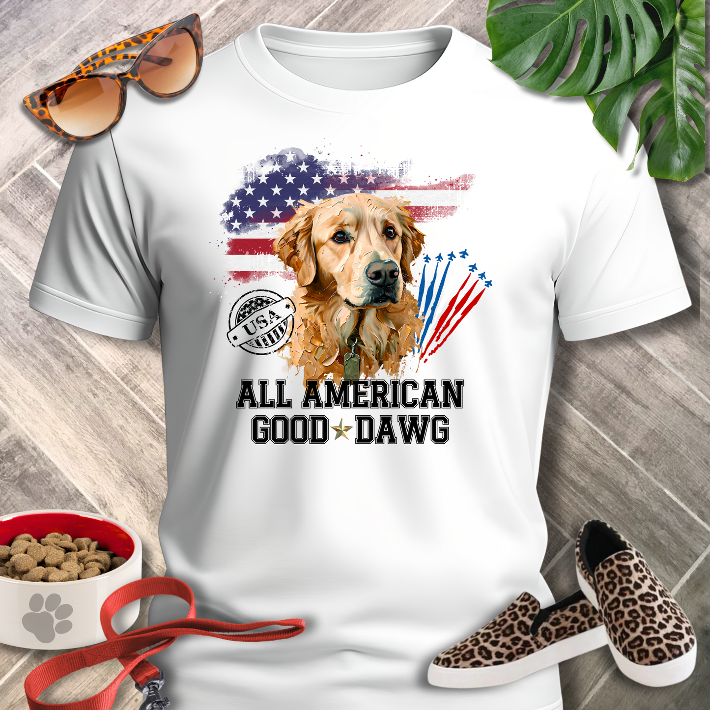 White t-shirt with a dog graphic and text, surrounded by sunglasses, shoes, and pet accessories on a wooden surface.