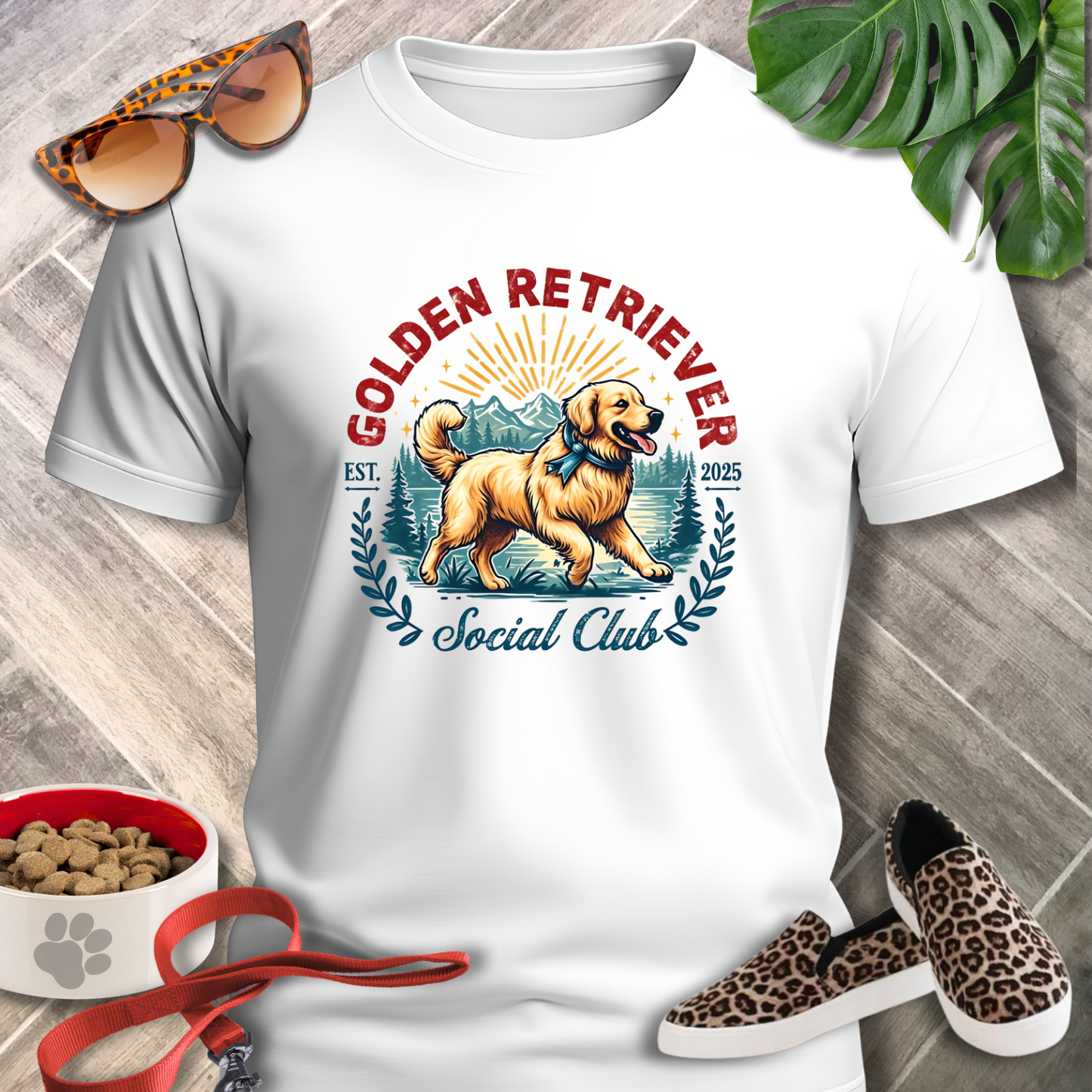 White t-shirt with Golden Retriever design, sunglasses, shoes, and pet accessories on a wooden surface.
