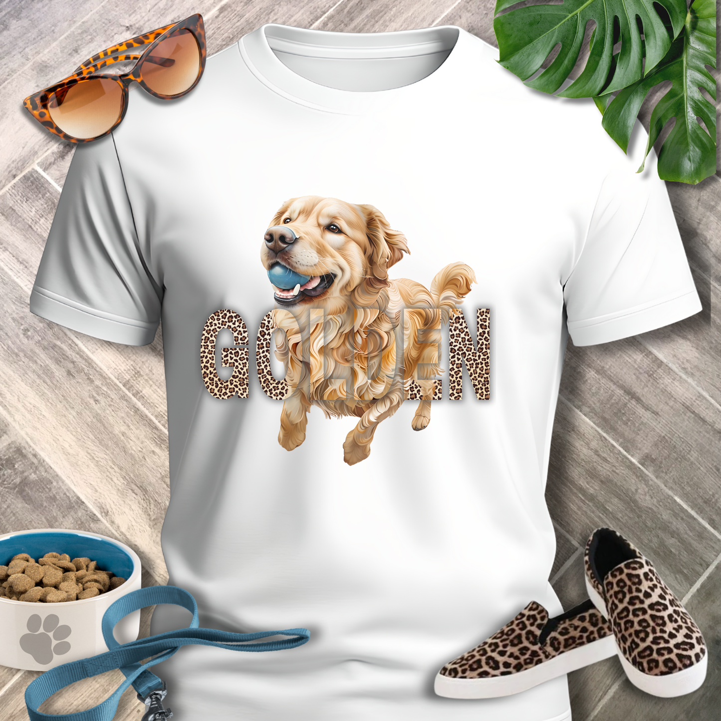 White t-shirt with a dog graphic and 'Good Boy' text, surrounded by sunglasses, shoes, and pet accessories on a wooden surface.