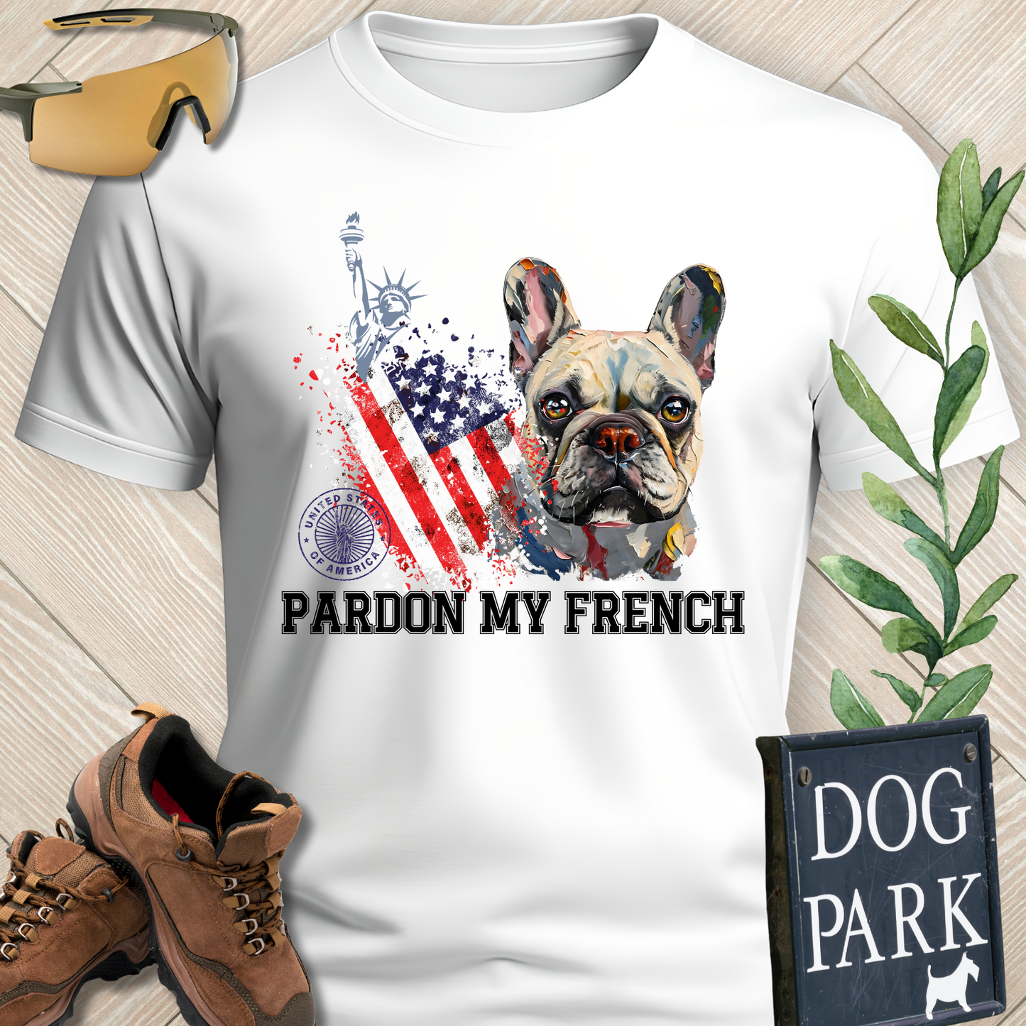 White t-shirt with a dog graphic and 'Pardon My French' text, surrounded by hiking boots and a 'Dog Park' sign.