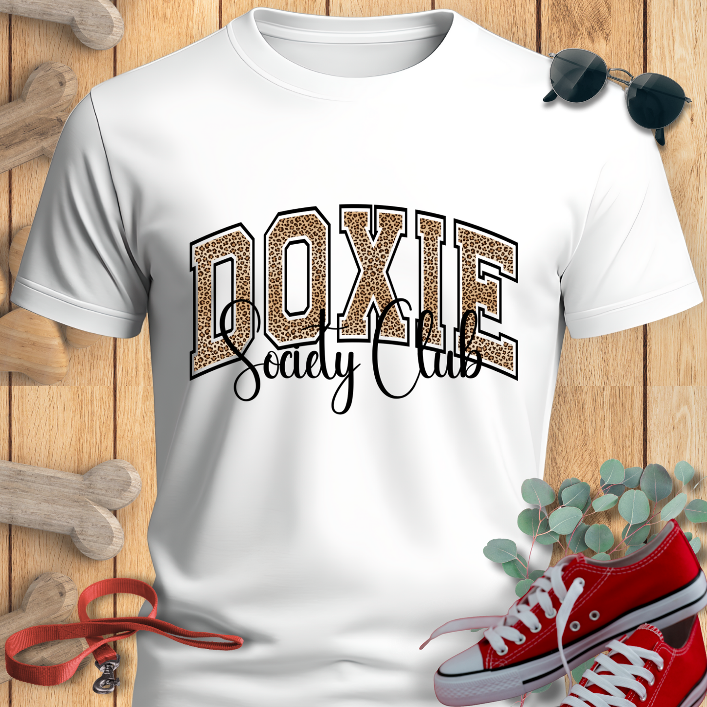 White t-shirt with 'Doxie Society Club' design on a wooden surface with red sneakers and sunglasses.