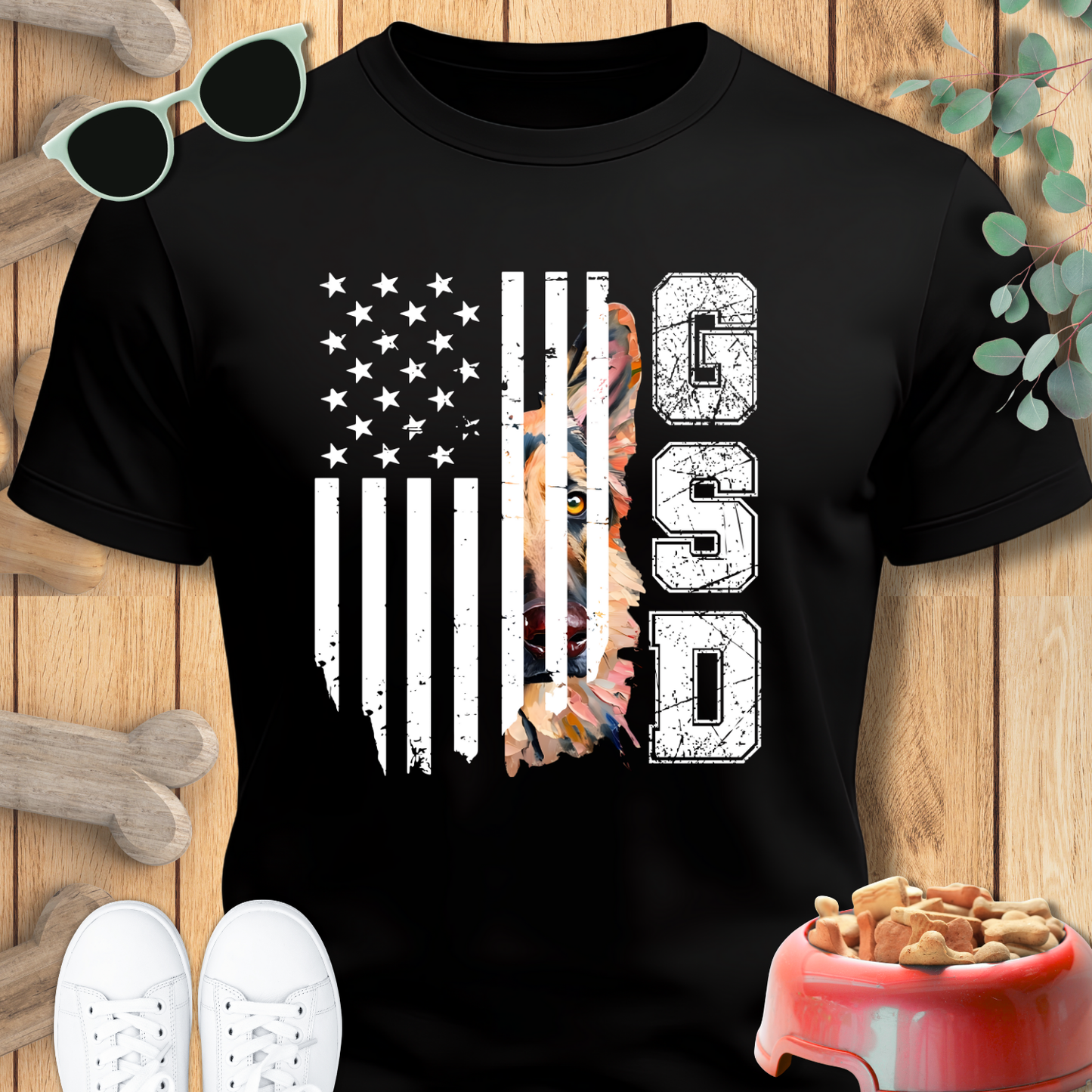 Black t-shirt with American flag and dog graphic on a wooden surface with shoes and a bowl.