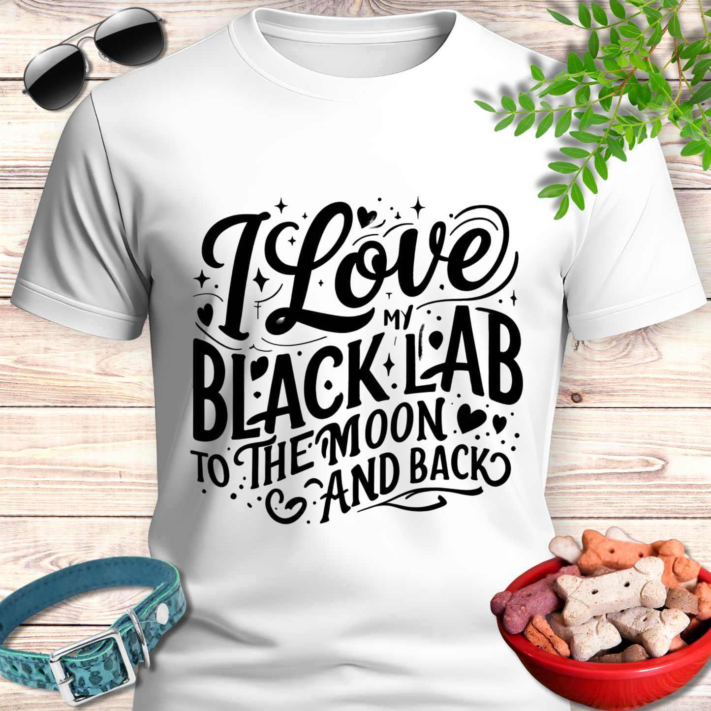 White t-shirt with 'I Love My Black Lab To The Moon And Back' text, sunglasses, dog collar, and treats on a wooden surface.