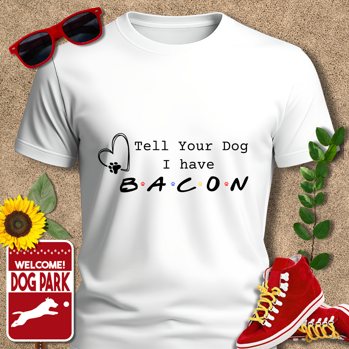 White t-shirt with 'Tell Your Dog I have Bacon' text, surrounded by sunglasses, sneakers, a sunflower, and a 'Welcome to the Dog Park' sign.
