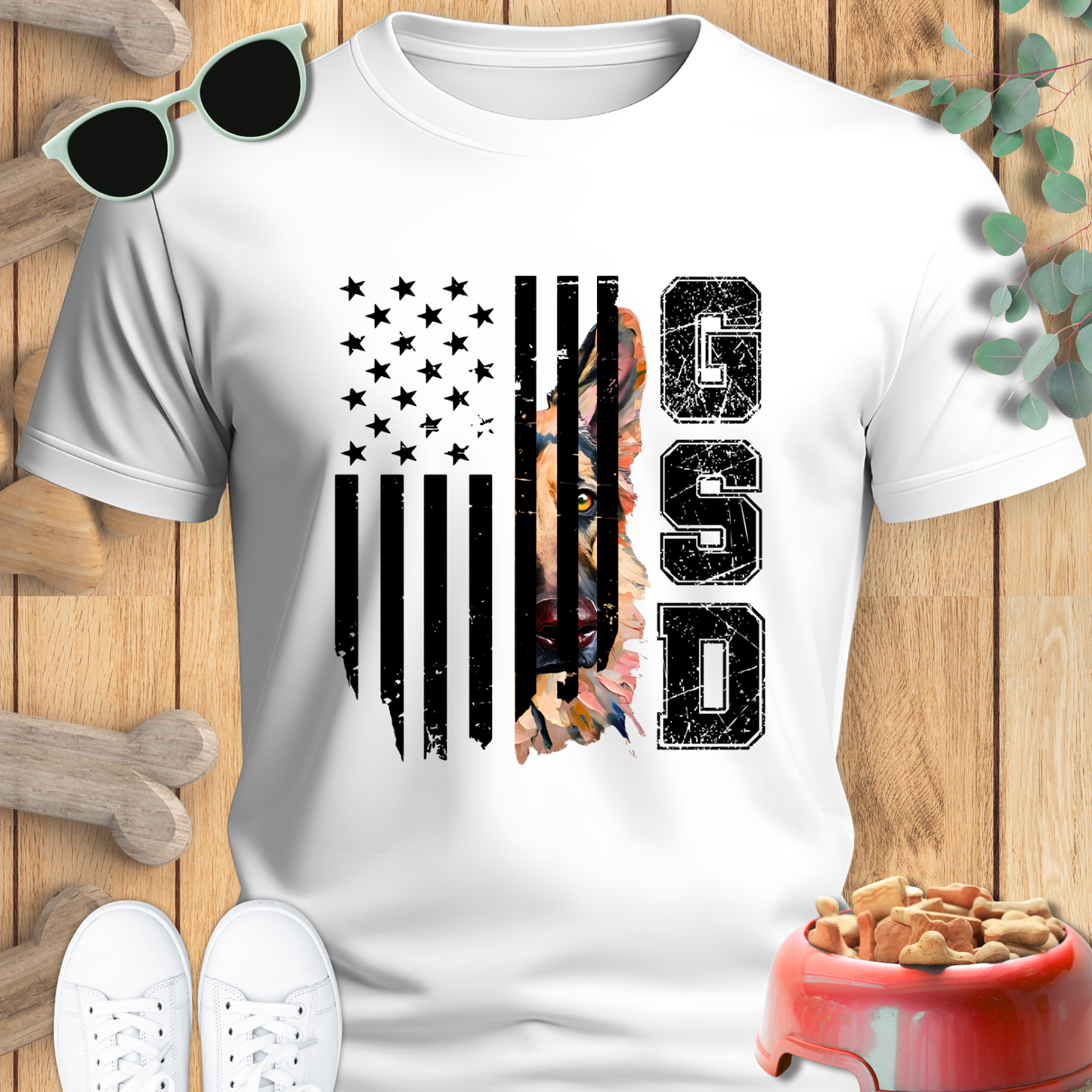 White t-shirt with American flag and 'GSD' design on a wooden surface with sunglasses and dog toys.