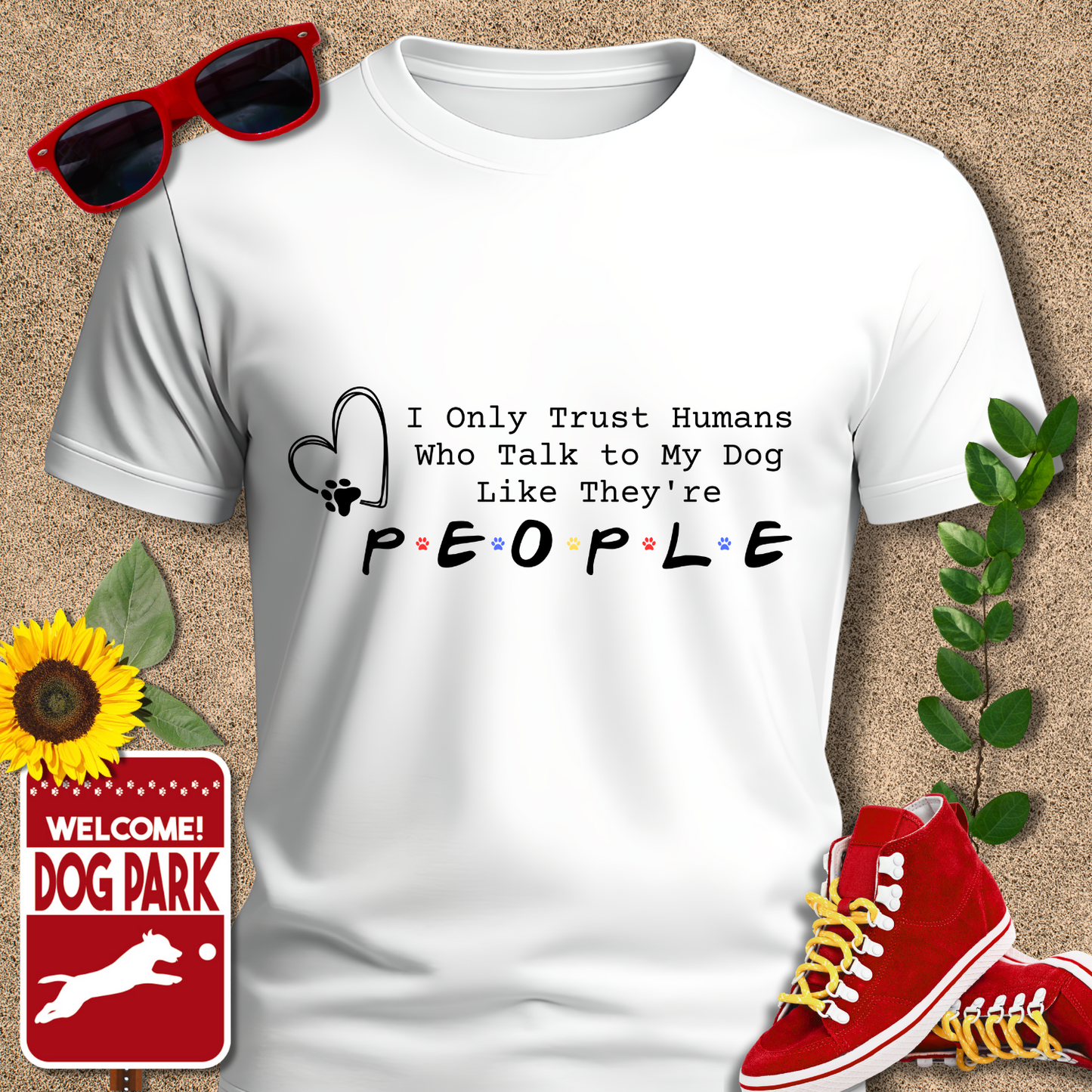 White t-shirt with humorous text design, sunglasses, sneakers, sunflower, and 'Dog Park' sign on a textured background.