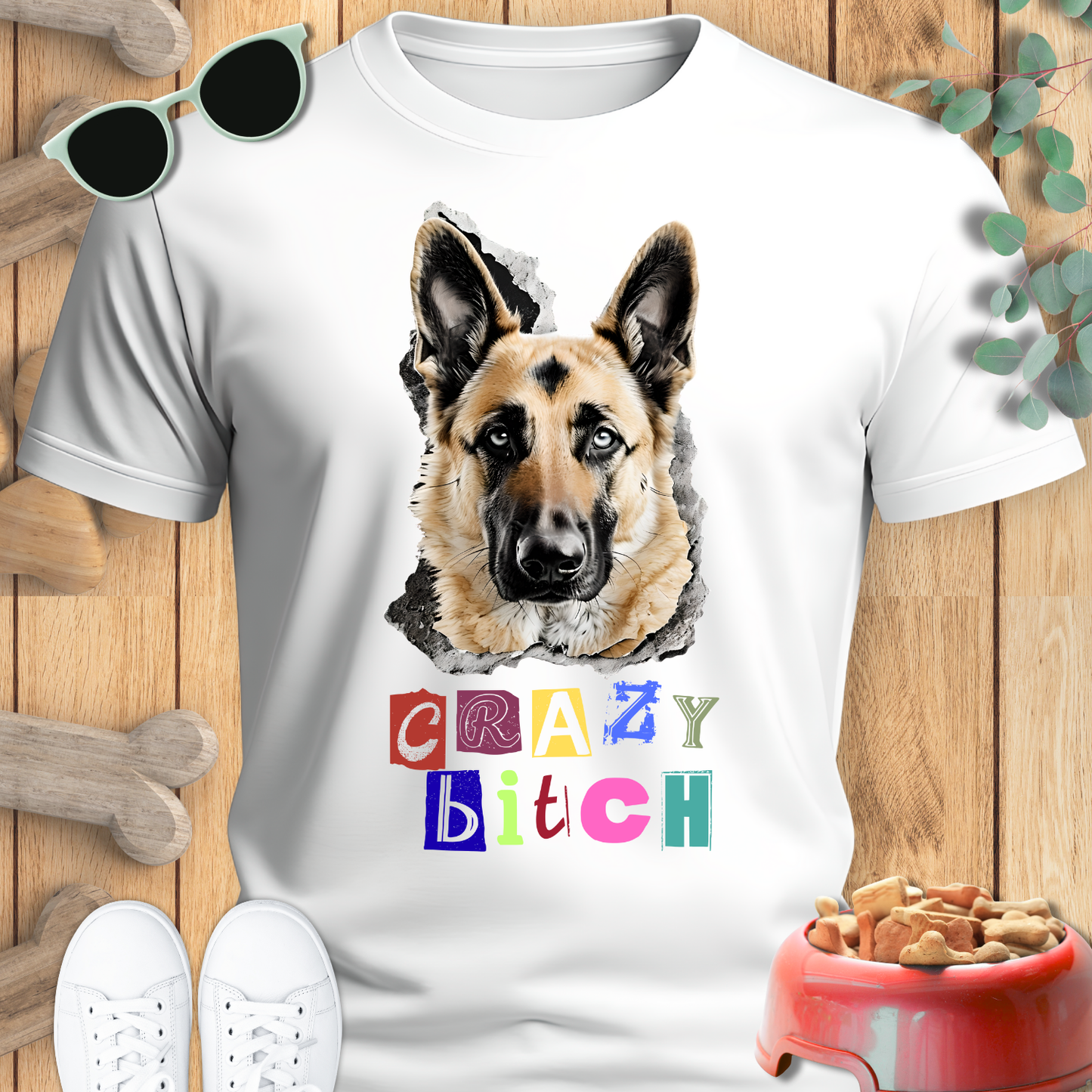 White t-shirt with a German Shepherd graphic and colorful text on a wooden surface with pet accessories.