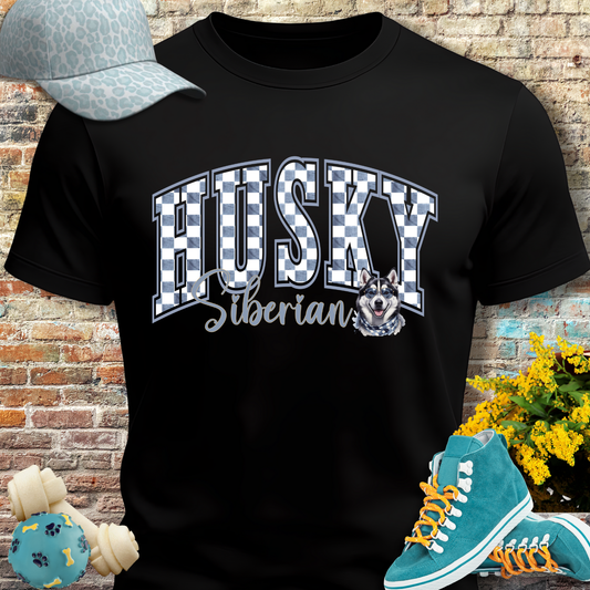 Black t-shirt with 'HUSKY Siberian' design, blue sneakers, and a cap on a brick wall background.