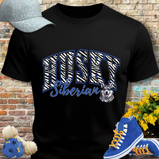 Black t-shirt with 'Husky Siberian' design, blue sneakers, cap, and dog toys against a brick wall.