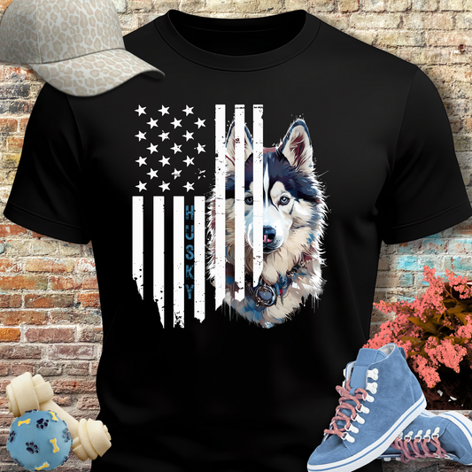 Black t-shirt with husky design and American flag, placed against a brick wall with shoes and a cap on either side.