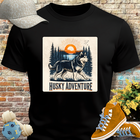 Black t-shirt with husky graphic and 'Husky Adventure' text, placed on a brick wall background.