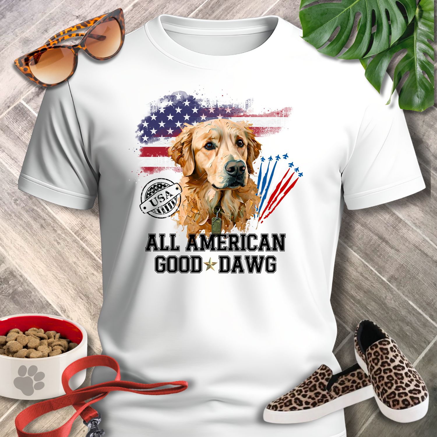 White t-shirt with a dog graphic and text, surrounded by sunglasses, shoes, and pet accessories on a wooden surface.