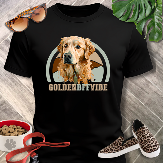 Black t-shirt with a dog graphic and 'GOLDENBFFVIBE' text, surrounded by pet accessories on a wooden surface.