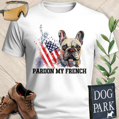 White t-shirt with a dog graphic and 'Pardon My French' text, surrounded by hiking boots and a 'Dog Park' sign.