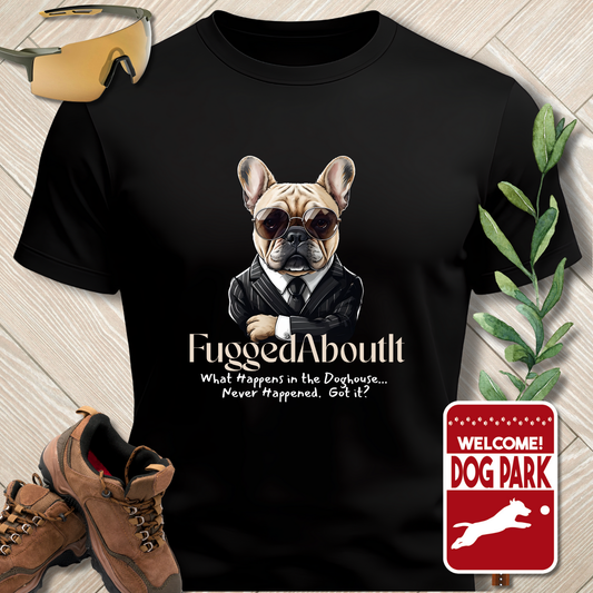 Black t-shirt with a dog graphic and text, placed on a wooden surface with shoes and a plant.