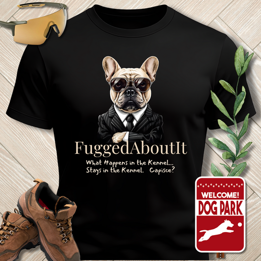 Black t-shirt with a dog graphic and text, placed on a wooden surface with shoes and a plant.