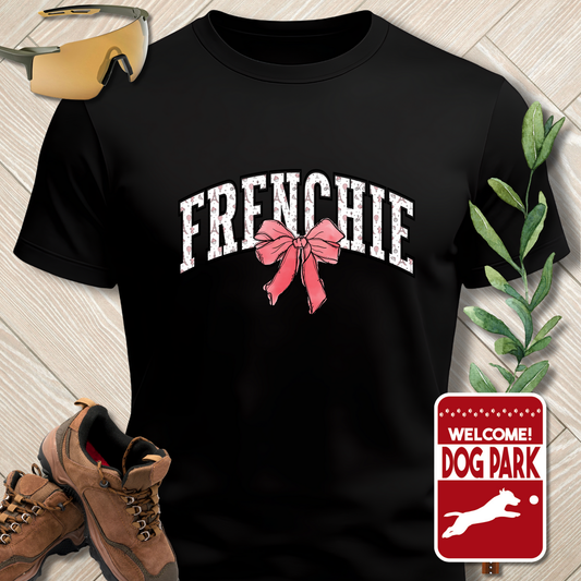 Black t-shirt with 'FRENCHIE' and a pink bow graphic, surrounded by hiking boots, sunglasses, and a 'Welcome to the Dog Park' sign.