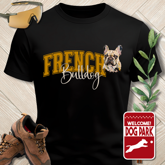 Black t-shirt with French Bulldog design and text, placed on a wooden surface with hiking boots and a 'Welcome to the Dog Park' sign.
