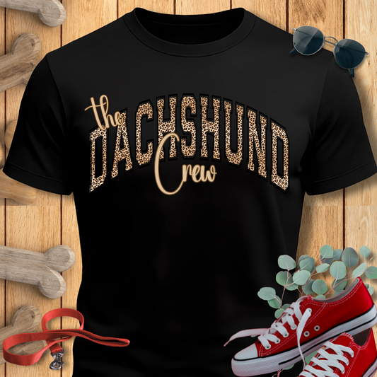 Black t-shirt with 'the DACHSHUND crew' text, red sneakers, and dog accessories on a wooden background