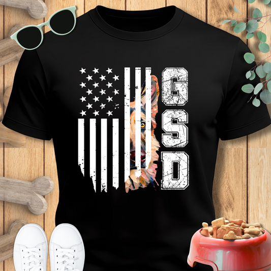 Black t-shirt with American flag and dog graphic on a wooden surface with shoes and a bowl.