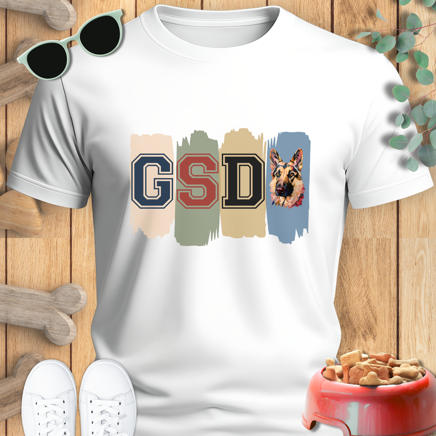 White t-shirt with 'GSD' design featuring a German Shepherd, sunglasses, shoes, and a dog bowl on a wooden surface.