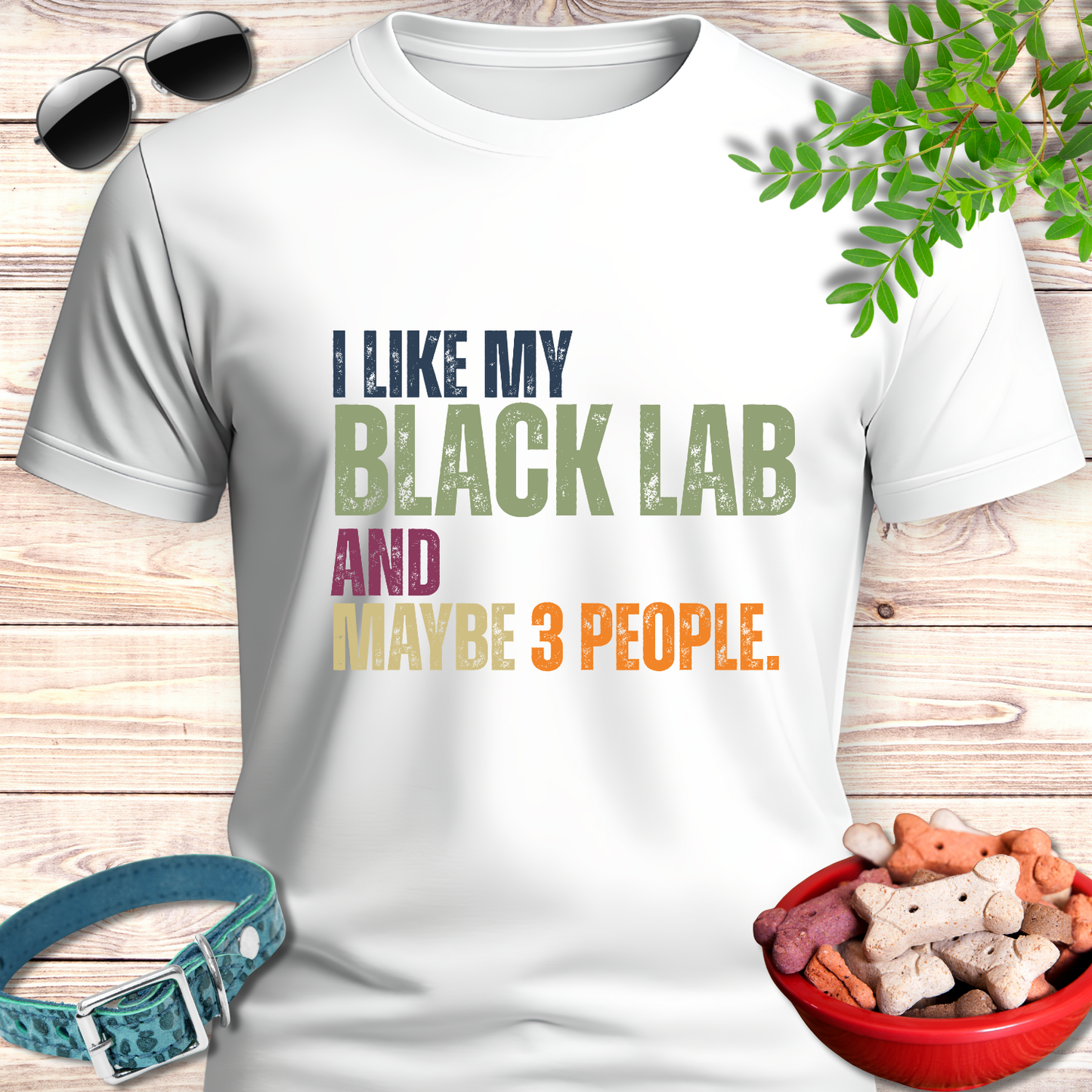 White t-shirt with text 'I like my Black Lab and maybe 3 people' on a wooden surface with pet accessories.