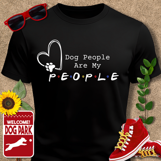 Black t-shirt with 'Dog People Are My People' text, sunglasses, red sneakers, sunflower, and 'Welcome to the Dog Park' sign on a beige background.