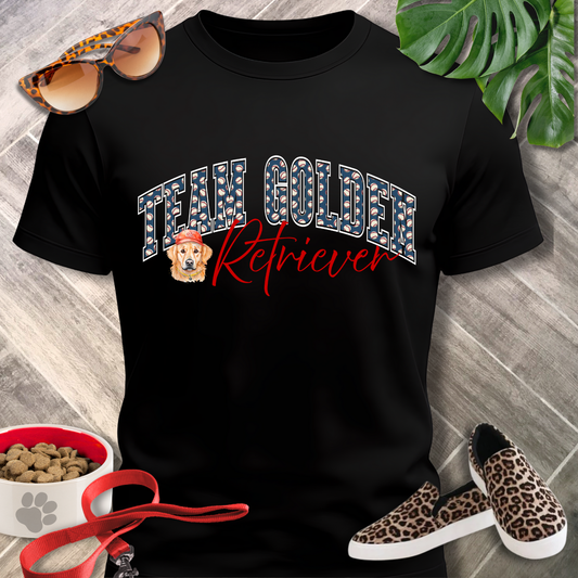 Black t-shirt with 'Team Golden Retriever' text, surrounded by sunglasses, pet food bowl, and leopard print shoes on a wooden surface.
