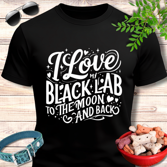 Black t-shirt with 'I Love My Black Lab To The Moon And Back' text on a wooden surface with pet accessories.