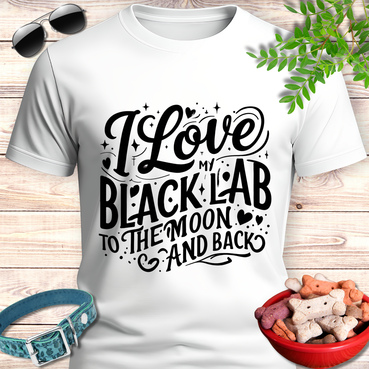 White t-shirt with 'I Love My Black Lab To The Moon And Back' text, sunglasses, dog collar, and treats on a wooden surface.