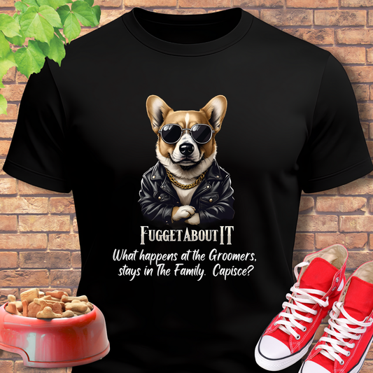 Corgi tshirt Fugget About It Groomers in Black with a corgi graphic and text, placed on a brick surface with red shoes and a dog bowl.