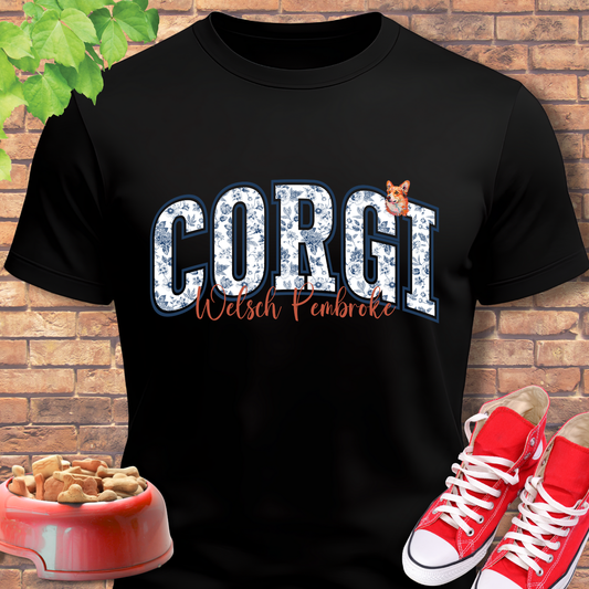 Black t-shirt with 'Corgi Welsh Pembroke' design, red shoes, and dog bowl on a brick background
