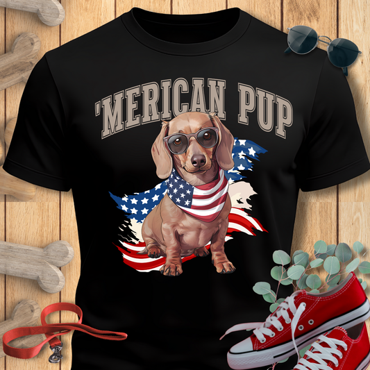 Dachshund shirt with 'Merican Pup in Black featuring a dachshund and American flag, displayed on a wooden surface with sneakers and a bone.