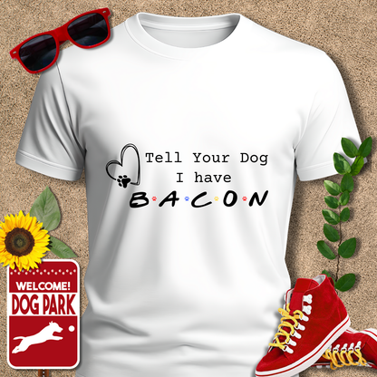 White t-shirt with 'Tell Your Dog I have Bacon' text, surrounded by sunglasses, sneakers, a sunflower, and a 'Welcome to the Dog Park' sign.