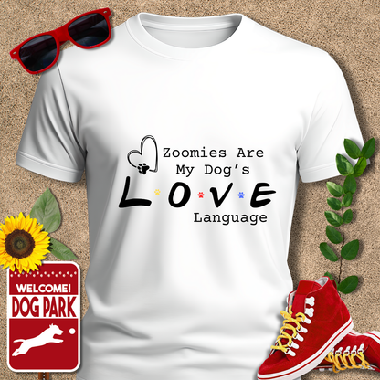White t-shirt with 'Zoomies Are My Dog's Love Language' text, surrounded by sunglasses, sneakers, a sunflower, and a 'Welcome to the Dog Park' sign.